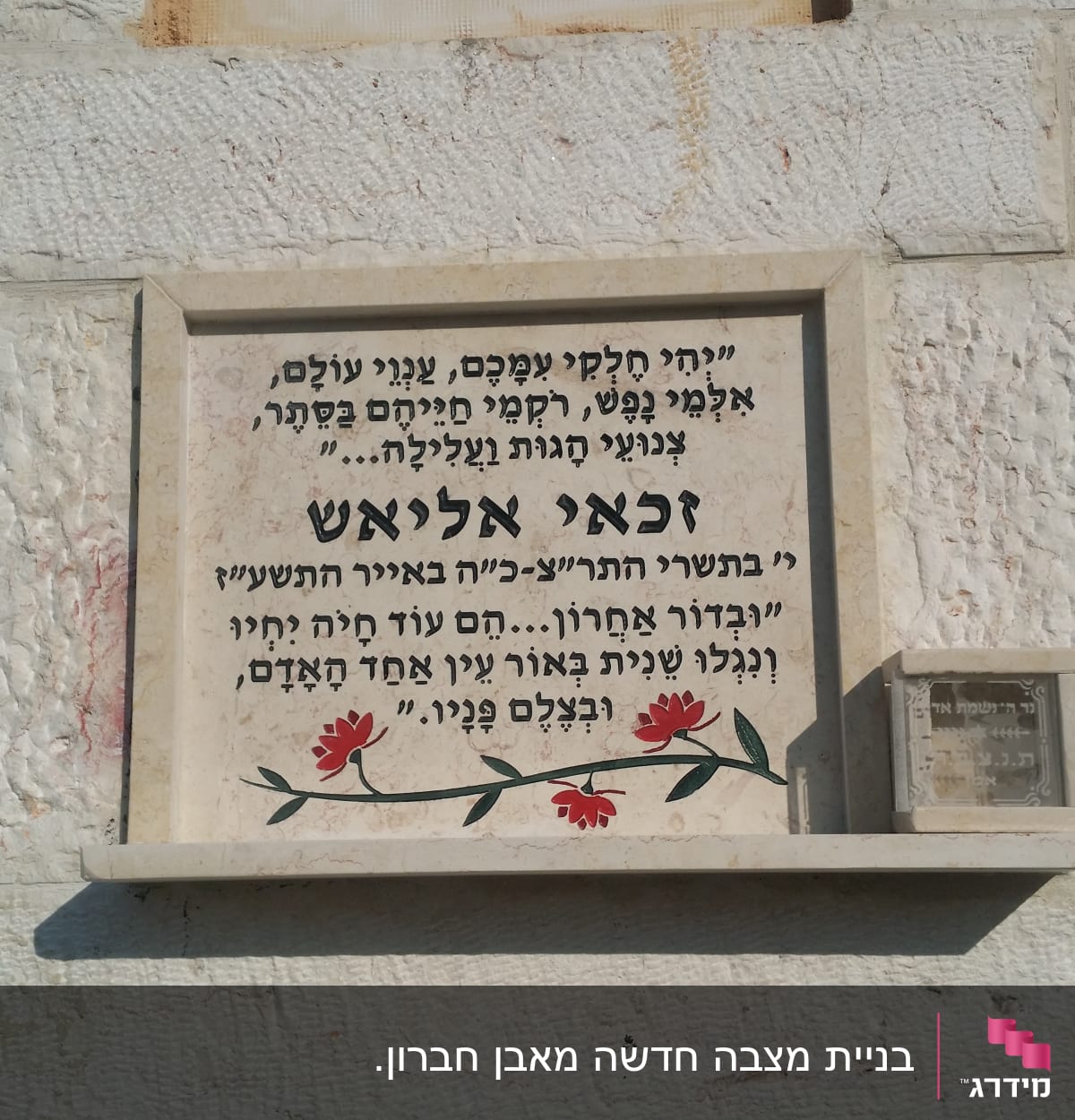 מצבה עם כיתוב בעברית ופרחים אדומים